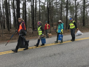 Photo of five people with high visibility gear, trash bags and buckets walking along the road.