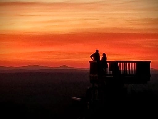 Sunset in orange with two figures in foreground overlooking the mountains to the north from the summit of Mount Agamenticus