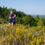 Two people running through shrubland on trail at the summit of Mount Agamenticus