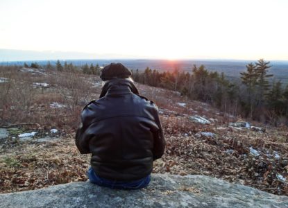 view from behind of a person sitting on a large rock on the Mount Agamenticus summit