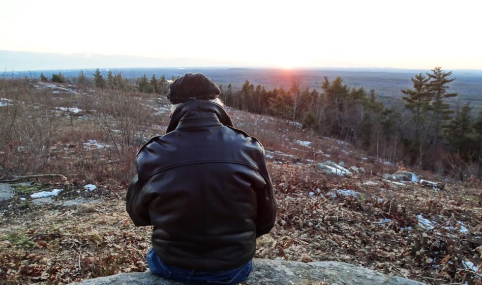 view from behind of a person sitting on a large rock on the Mount Agamenticus summit